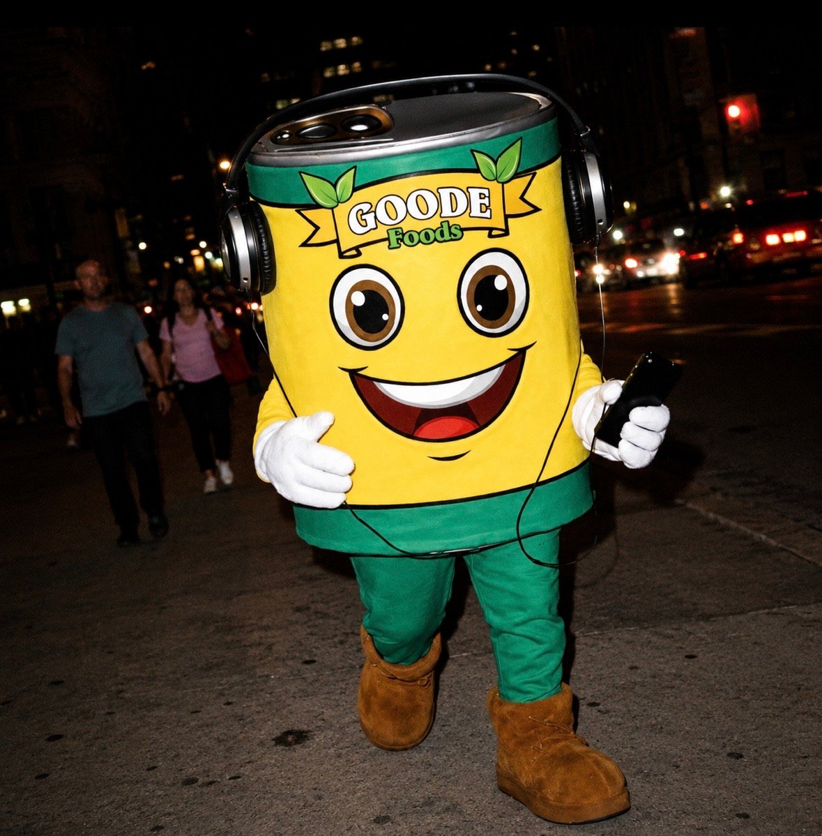 Goode Foods mascot wearing headphones on a city street at night